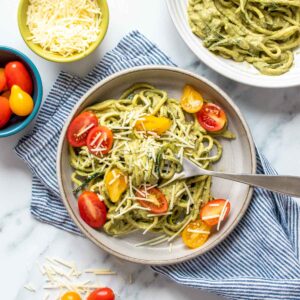 Pesto covered zucchini noodles topped with sliced tomatoes and parmesan on a grey plate with a fork on it