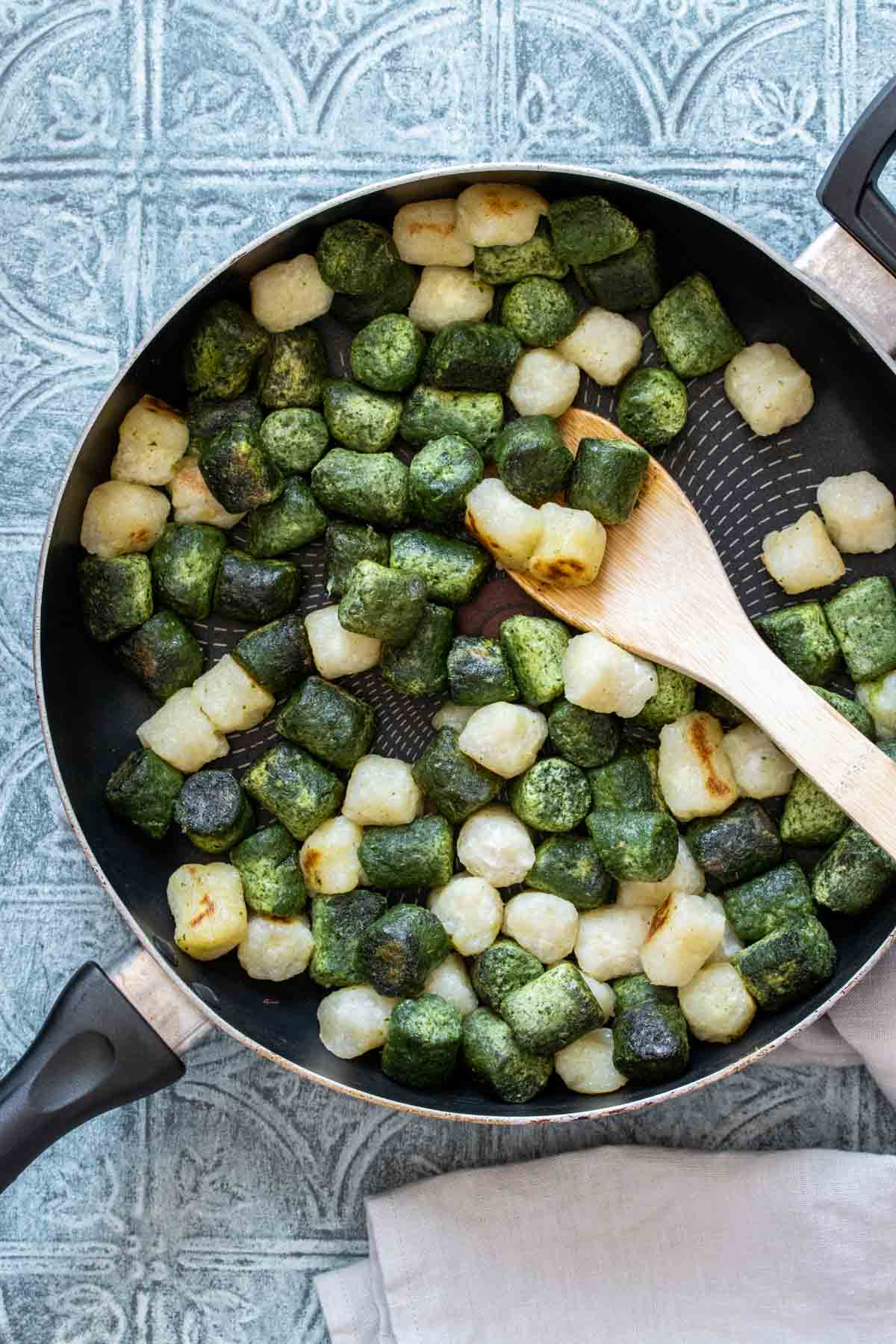 Top view of a wooden spoon mixing green and white gnocchi in a pan