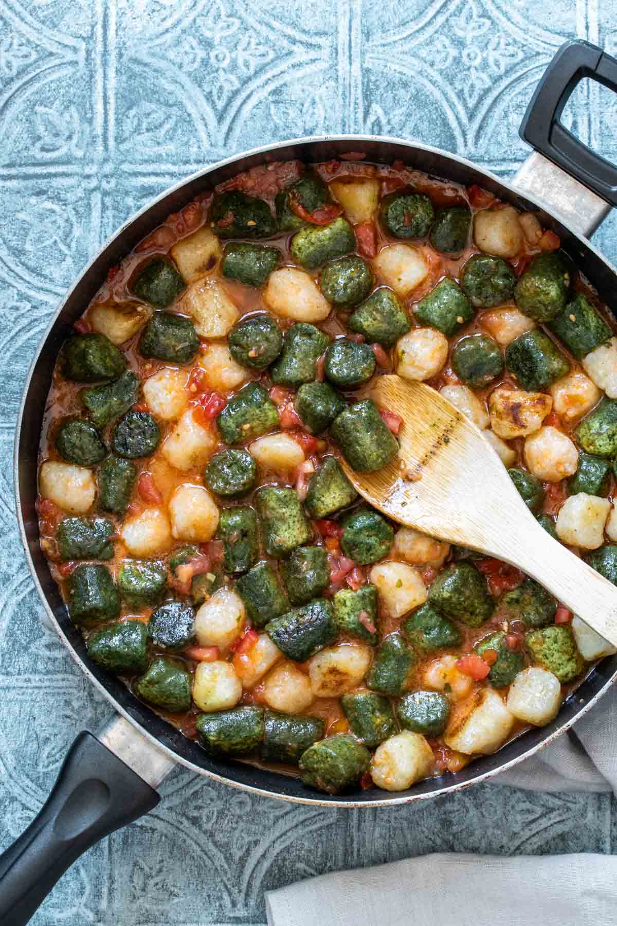 A wooden spoon mixing gnocchi and a red sauce in a pan