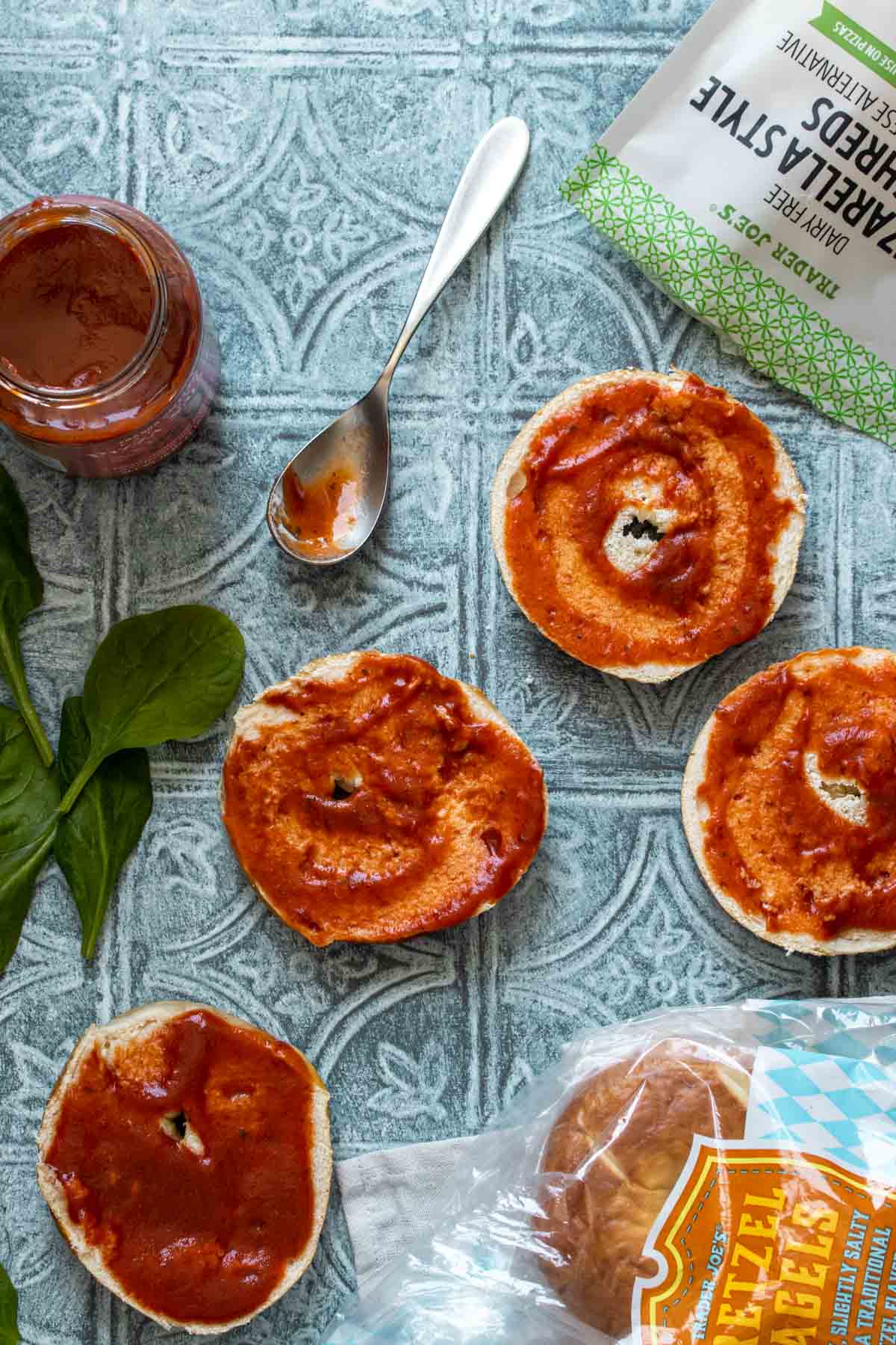 Cut bagels on a blue surface with pizza sauce on them