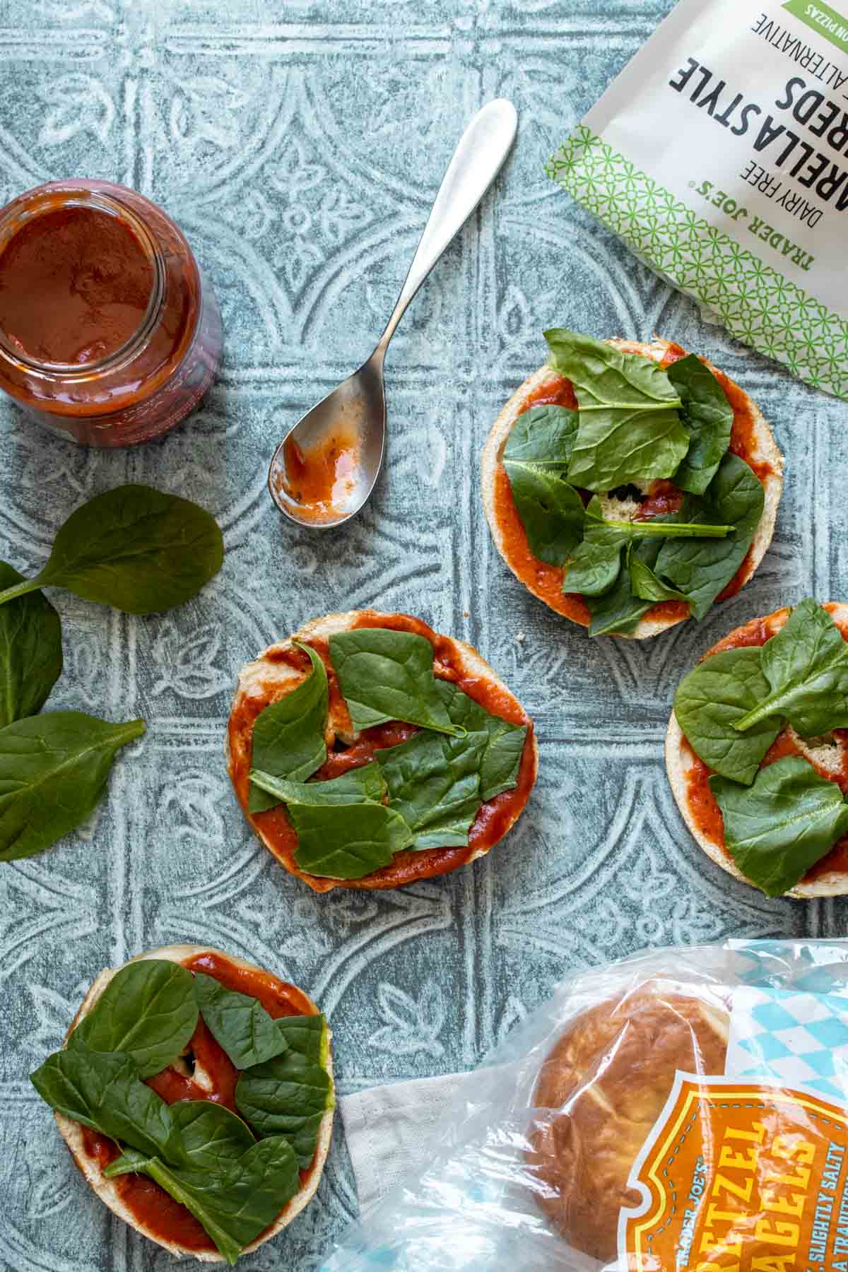 A blue surface with open faced bagels topped with pizza sauce and spinach