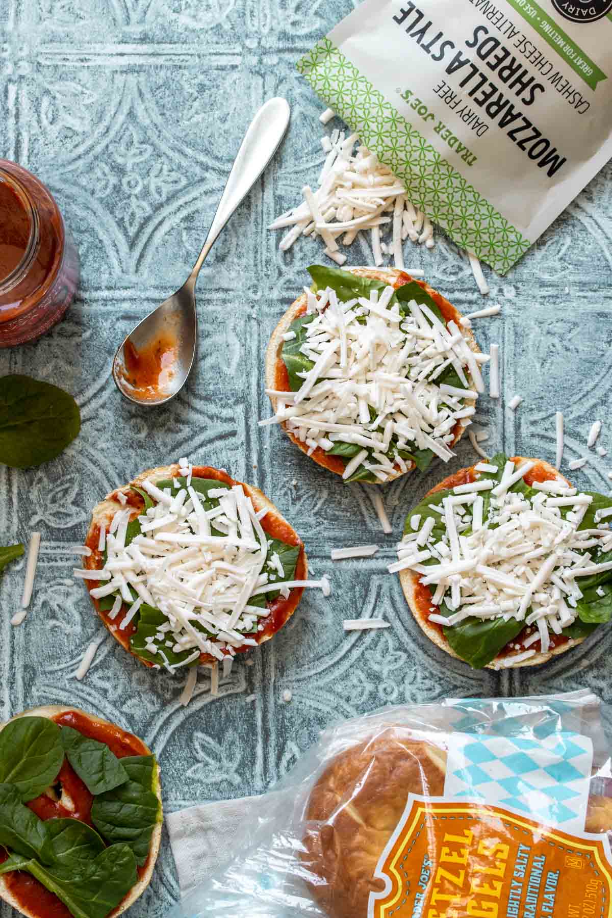 Bagels with pizza sauce, spinach and cheese sitting on a blue tiled surface