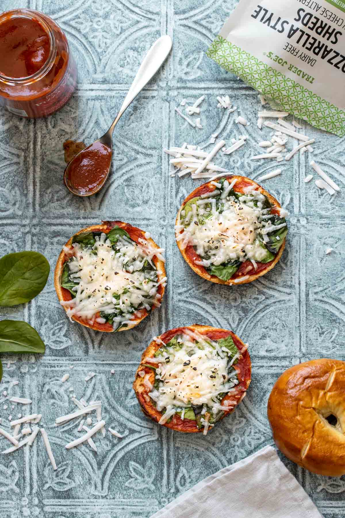 Bagels with pizza sauce, spinach and cheese that have been baked sitting on a blue tiled surface