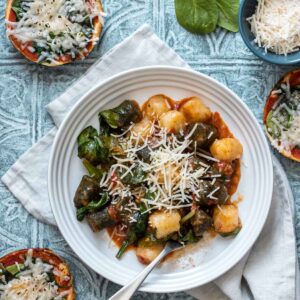 Green and white gnocchi and red sauce mixed with spinach and Parmesan in a white bowl.
