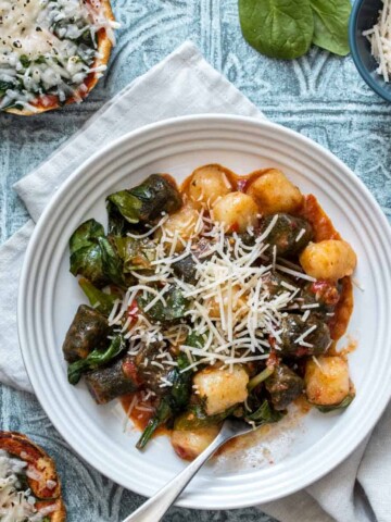 Green and white gnocchi and red sauce mixed with spinach and Parmesan in a white bowl.