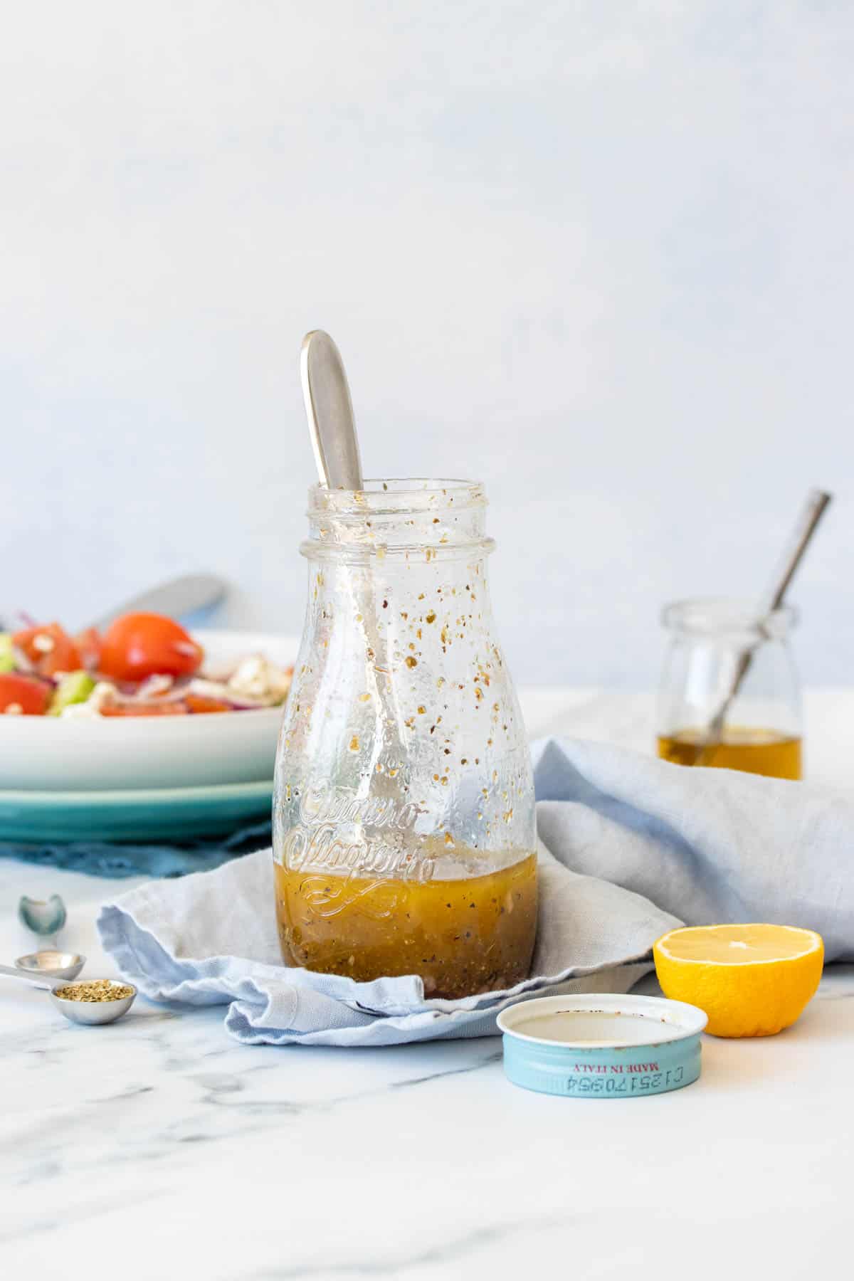A glass jar on a light blue towel on a marble surface that is partially filled with an olive oil and vinegar based dressing