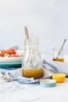 A glass jar with an olive oil and vinegar dressing and a fork in it sitting on a towel on a marble surface.