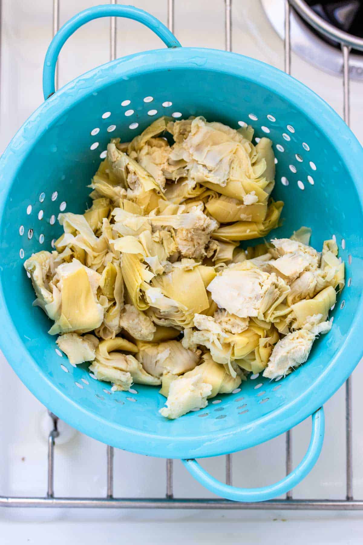 Artichoke hearts in a turquoise strainer sitting in a sink