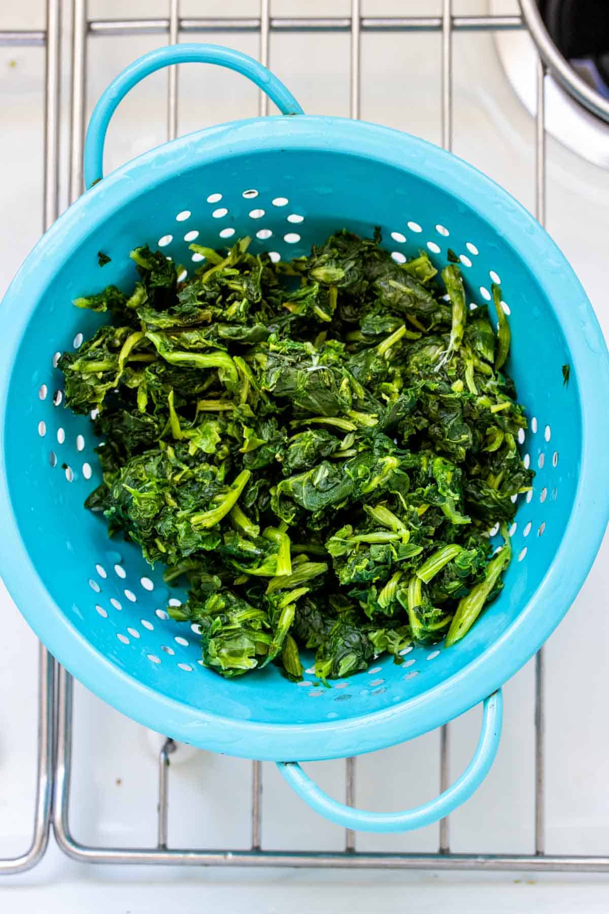 Top view of a turquoise strainer in a sink filled with chopped frozen spinach