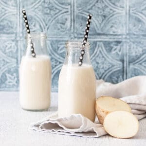 A potato cut in half next to a glass jar of milk on a grey towel in front of another jar on a kitchen counter