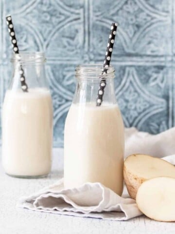 A potato cut in half next to a glass jar of milk on a grey towel in front of another jar on a kitchen counter