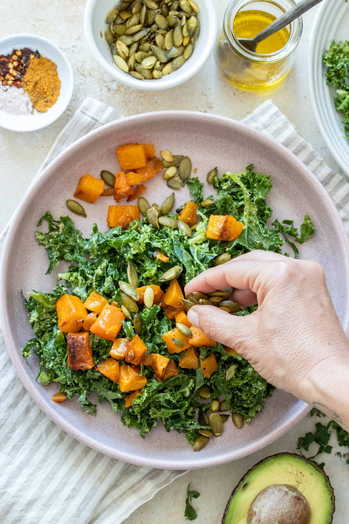 Hand putting pumpkin seeds on a kale and butternut squash salad in a pink plate