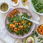 A salad with butternut squash and kale on a striped towel with ingredients for it around it