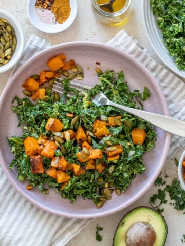 A salad with butternut squash and kale on a striped towel with ingredients for it around it