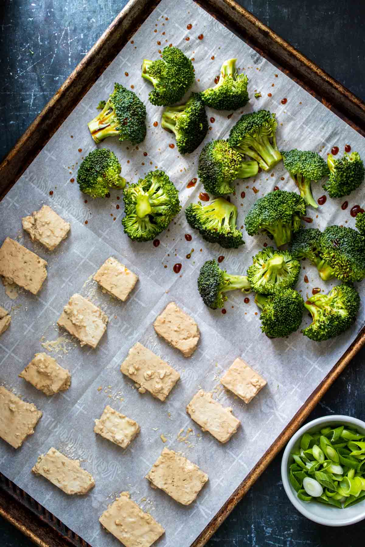 A baking sheet with parchment paper topped with tofu and pieces of broccoli