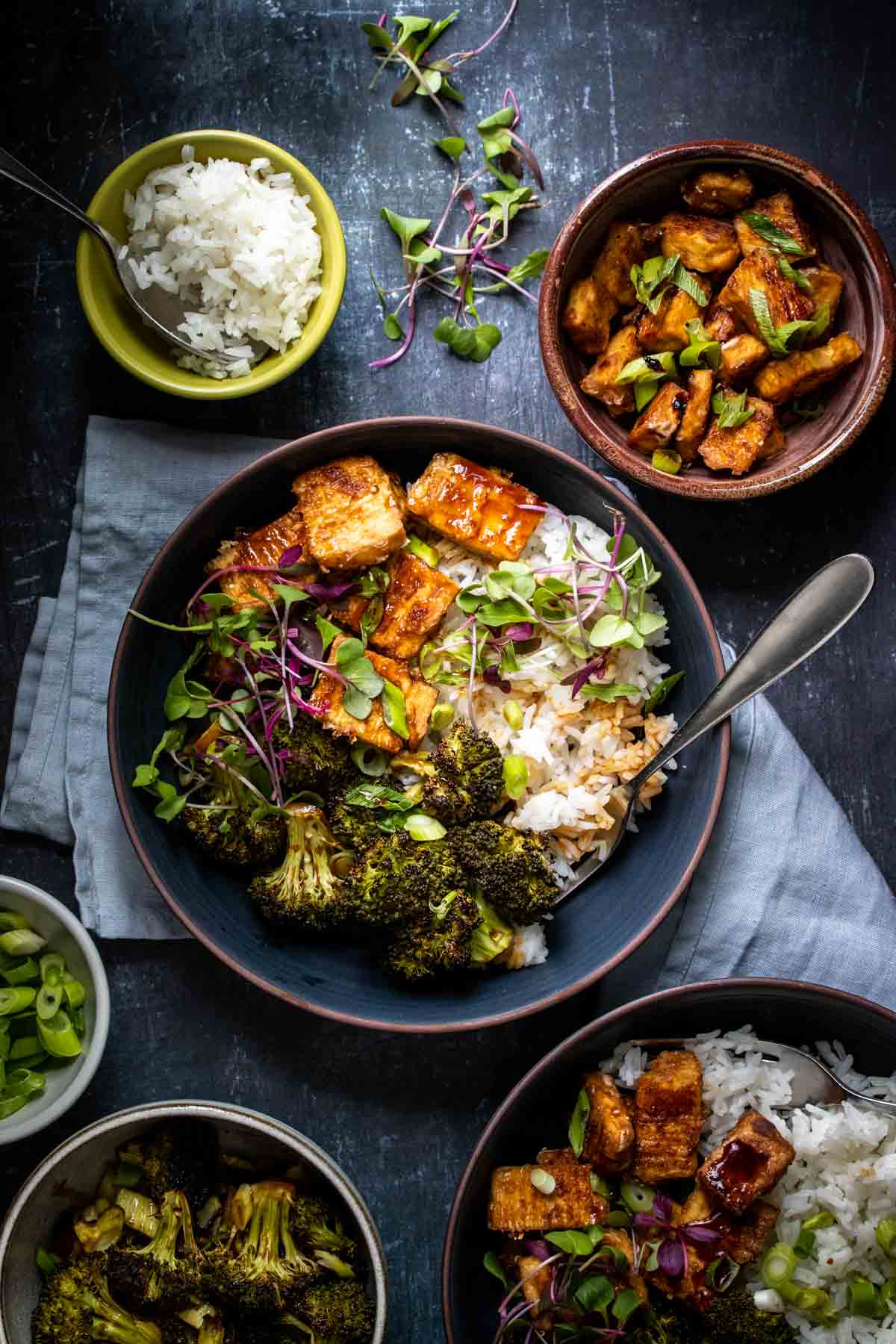 A fork in a bowl of rice, broccoli and crispy tofu with teriyaki sauce over it