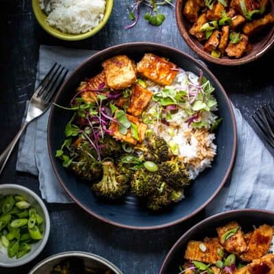Teriyaki tofu and broccoli sprinkled with green onions and microgreens over rice in a dark blue bowl