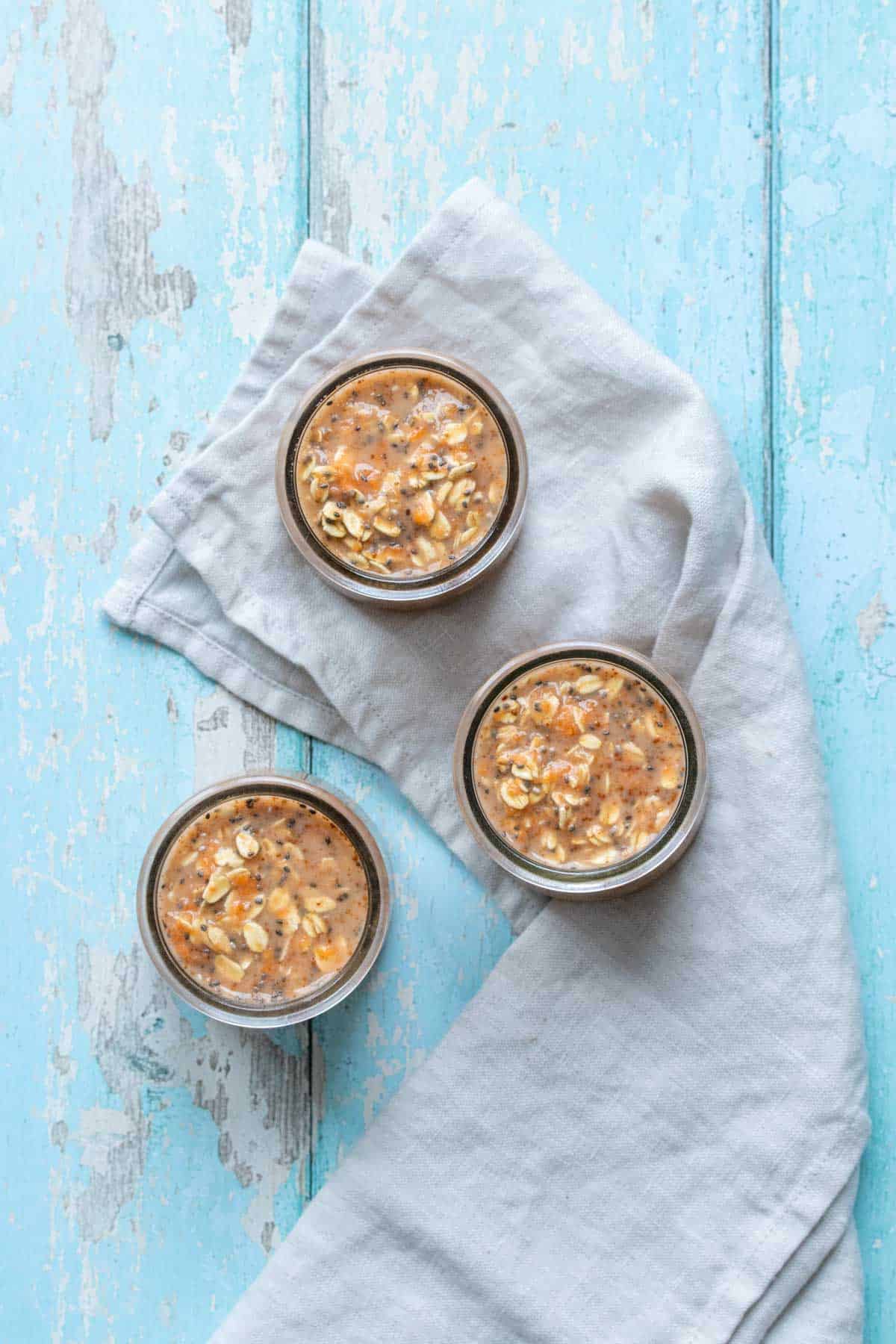 Top view of three jars filled with an oats and carrot mixture on a blue wooden surface