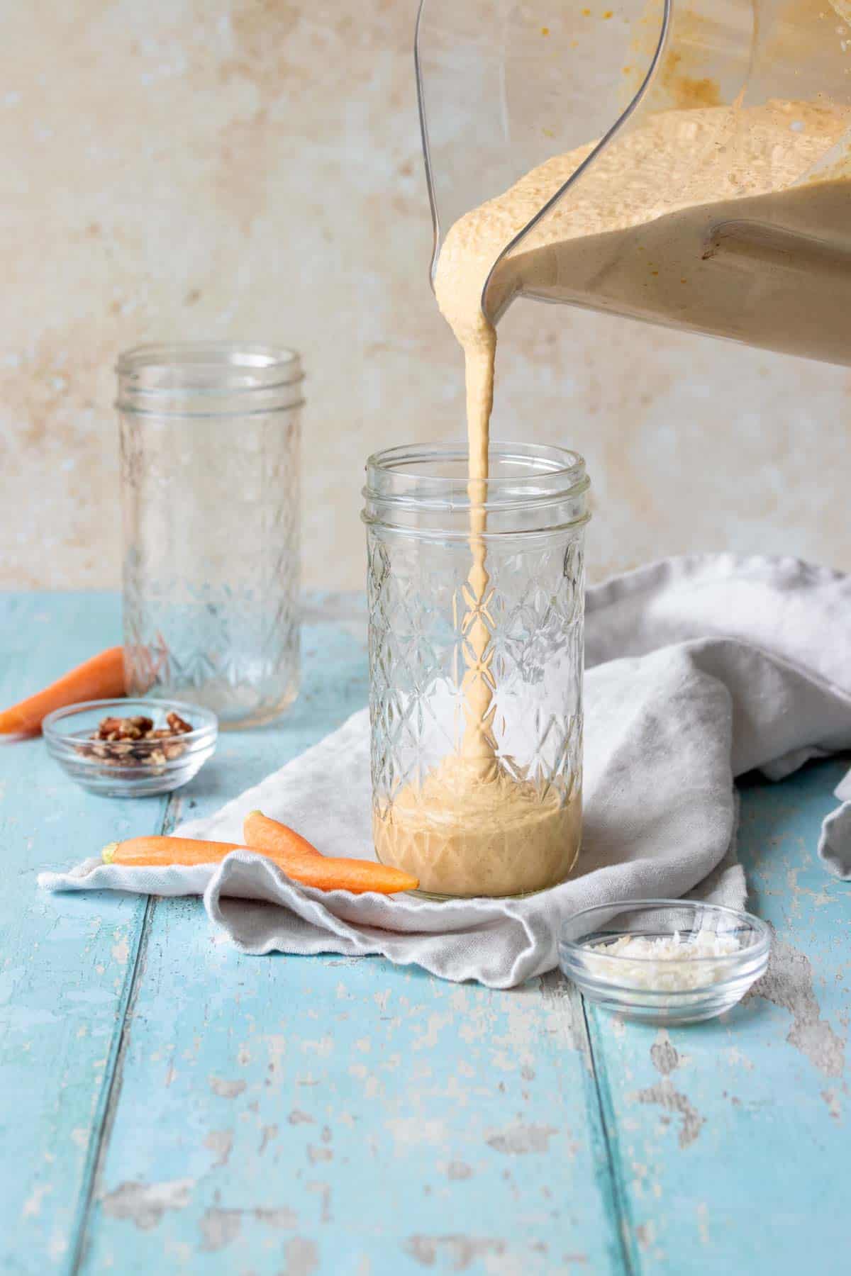 A blender pouring a peach colored smoothie into a glass jar on a blue wooden surface