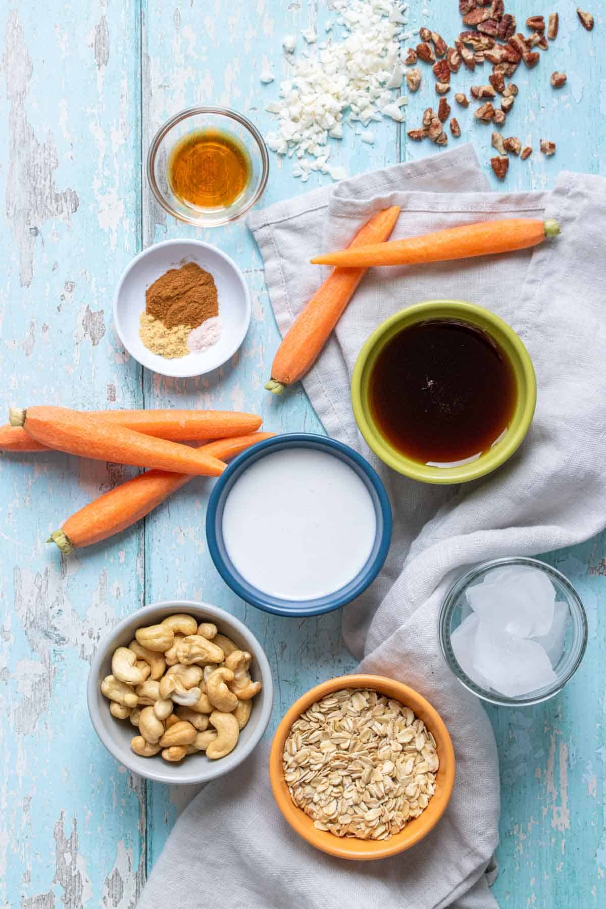 Top view of a blue wooden surface with ingredients on it to make a carrot cake cashew based smoothie