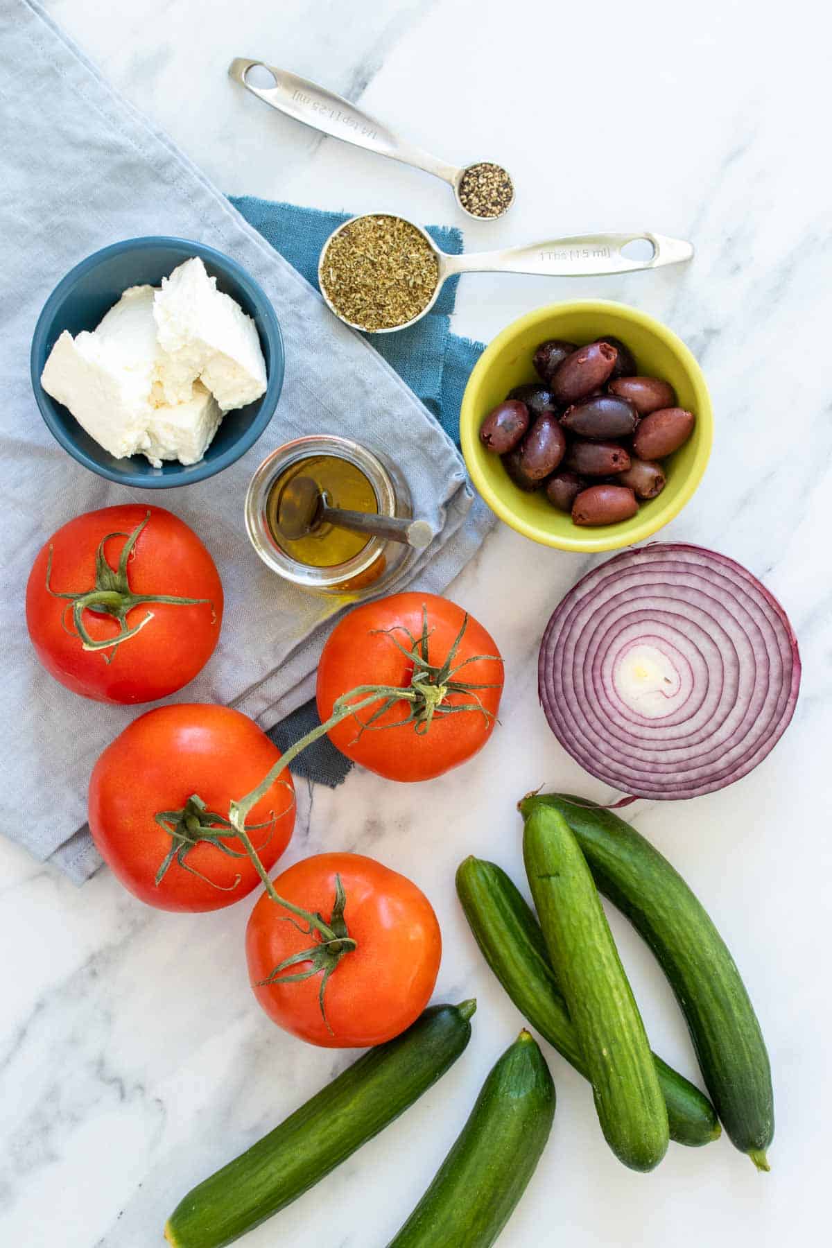 Tomatoes, cucumbers, onion, feta, olives, oil, pepper and oregano on a marble surface