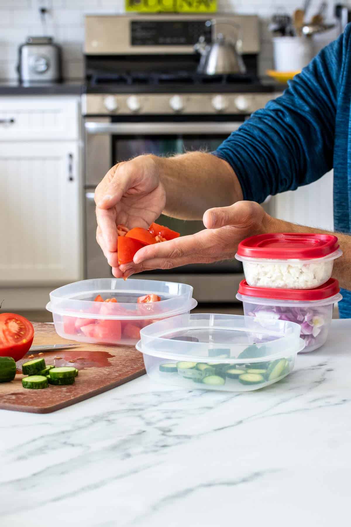 Hands putting cut tomatoes into a plastic container next to other containers filled with veggies