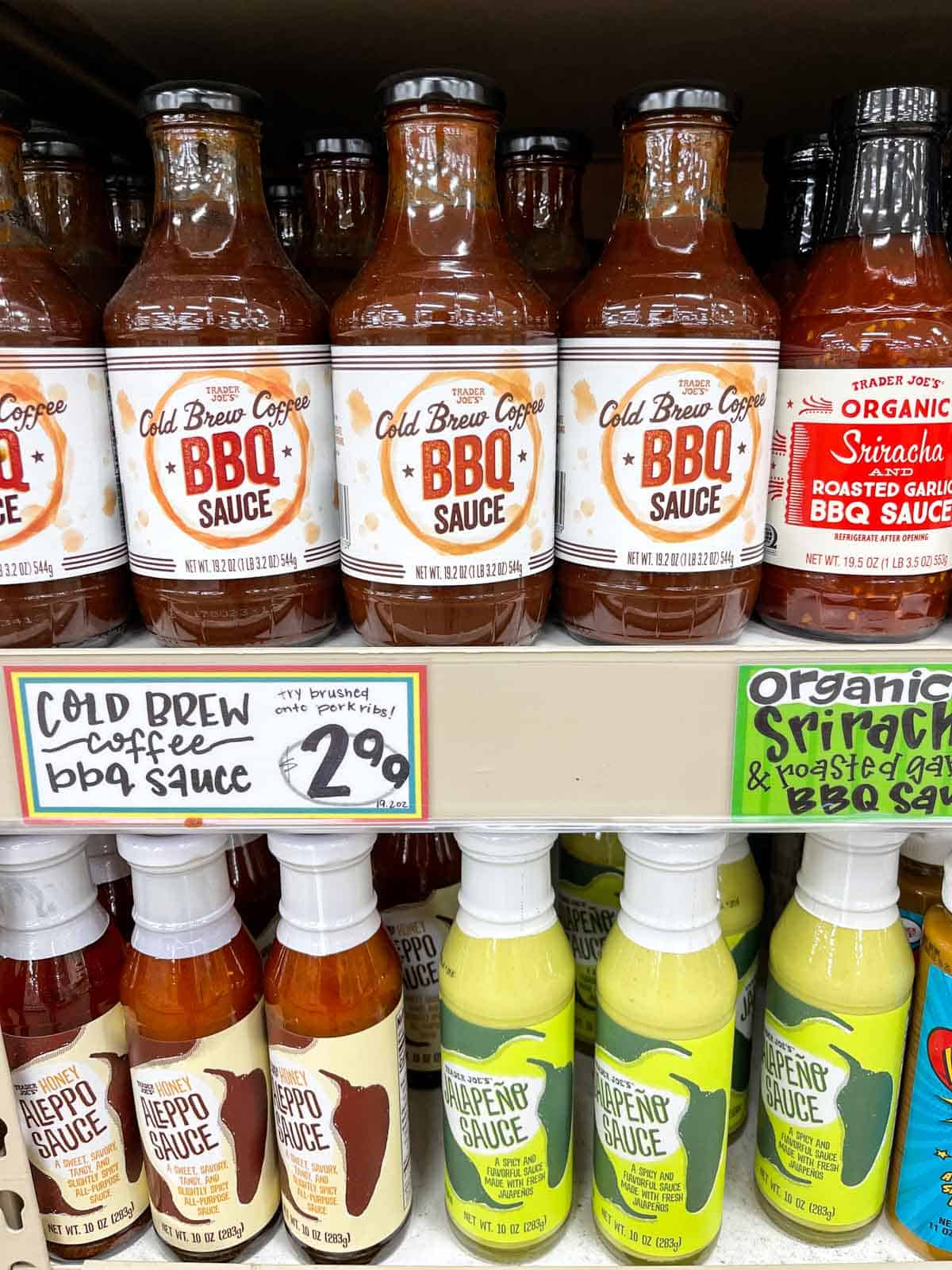 Two grocery store shelves with bottles of different types of sauces on them