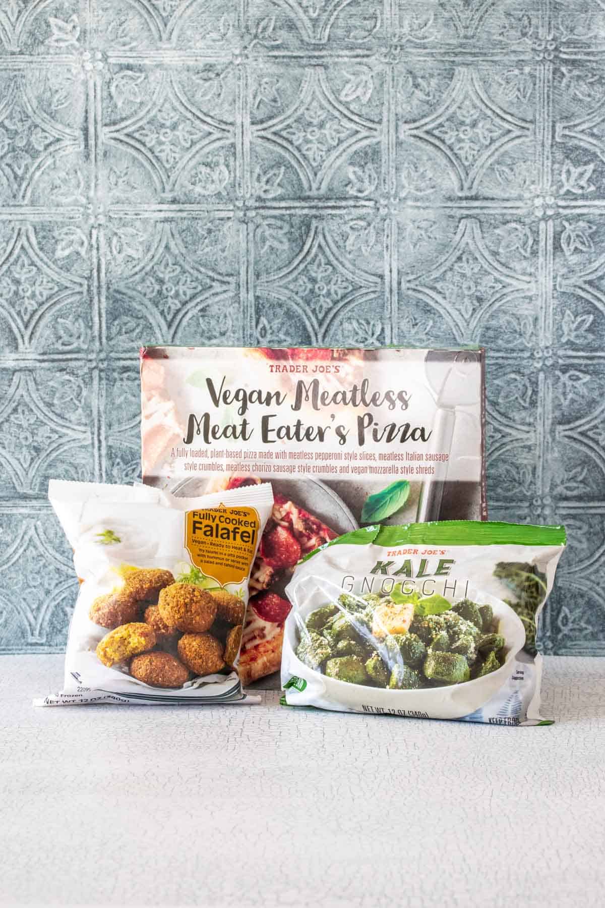 Bags of frozen ready food that is vegan on a white shelf with a blue tiled background