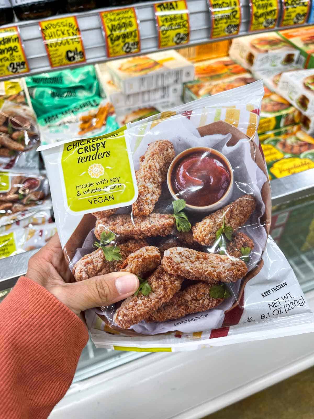 A hand holding a bag of vegan chickenless crispy tenders from the frozen section