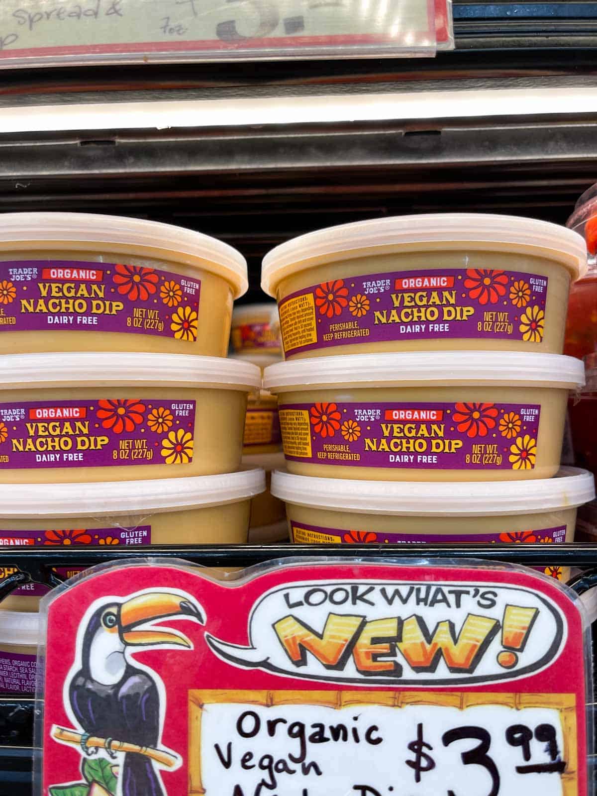 A stack of vegan cheese dip containers on the shelf of a grocery store