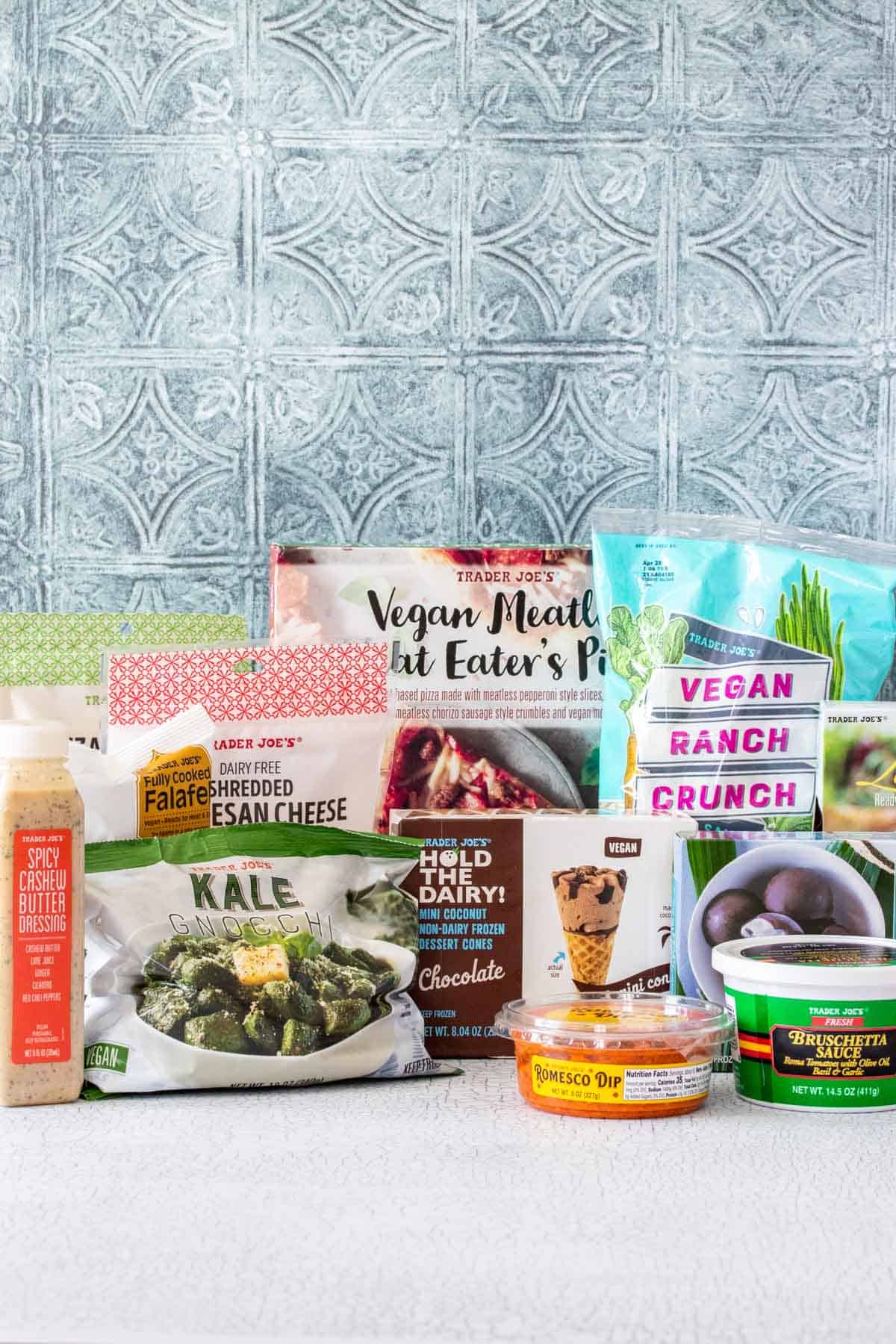 A collection of items from trader joe's that are labeled vegan sitting on a white counter with a blue tiled background