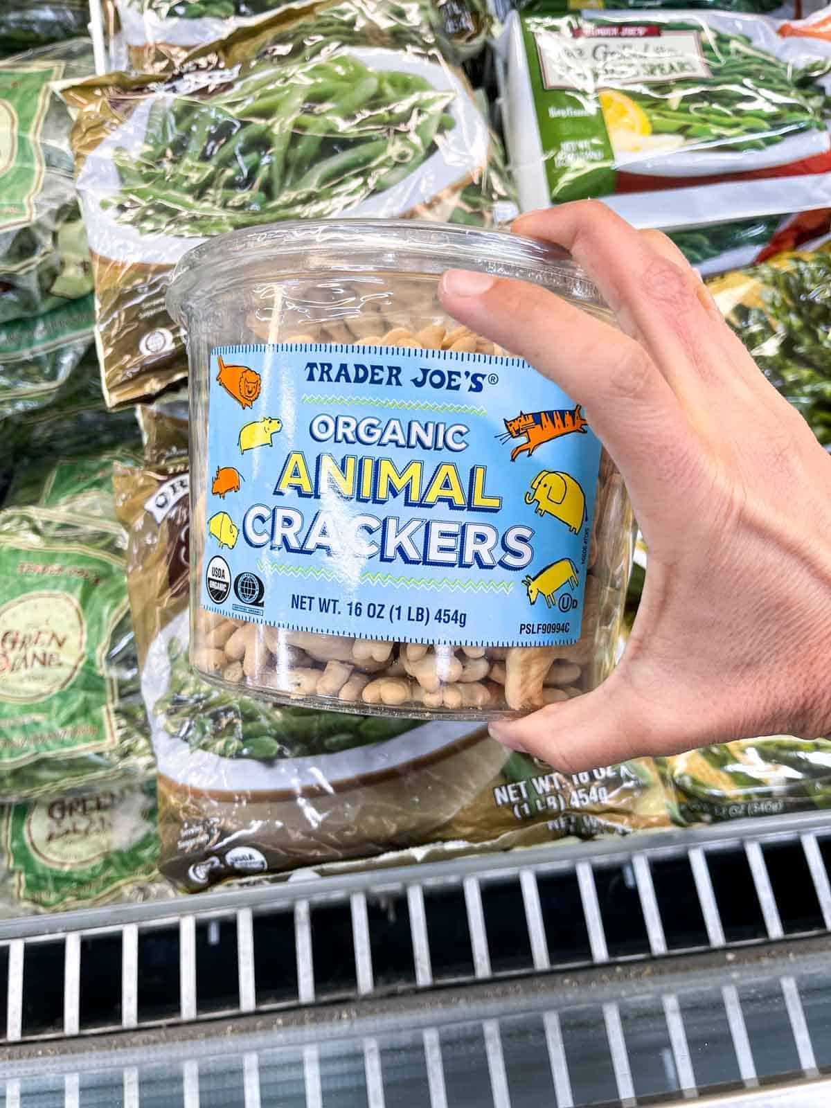 A hand holding a plastic package of animal crackers with a blue label