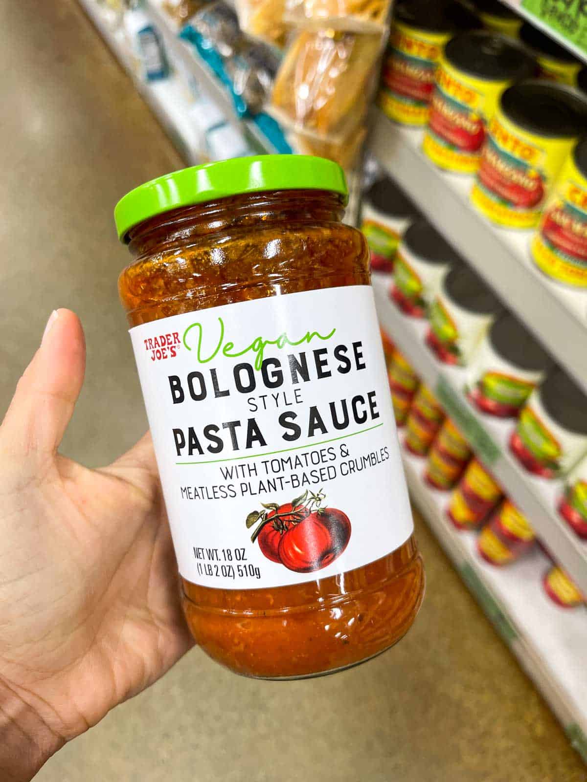 A hand holding a glass jar of Trader Joe's brand vegan bolognese pasta sauce