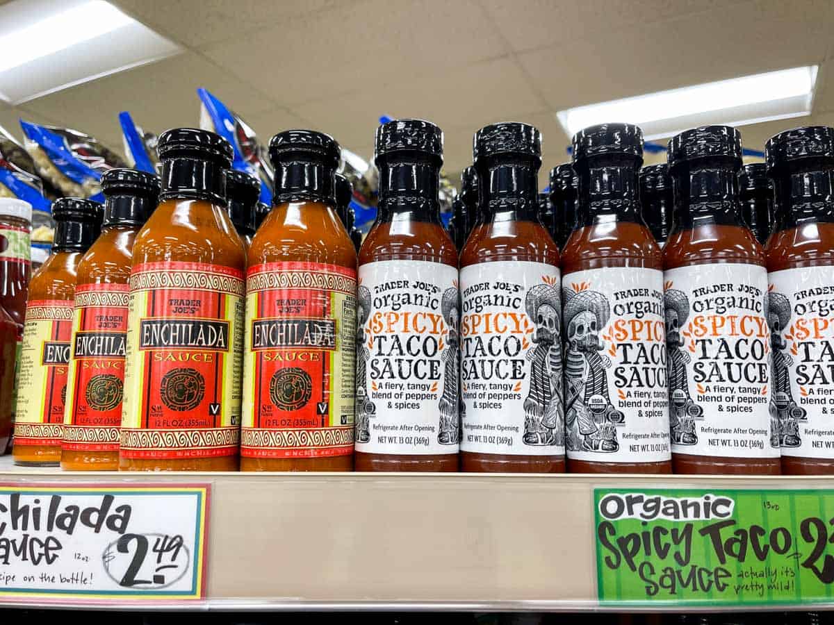 A shelf at a grocery store with a row of taco and enchilada sauces