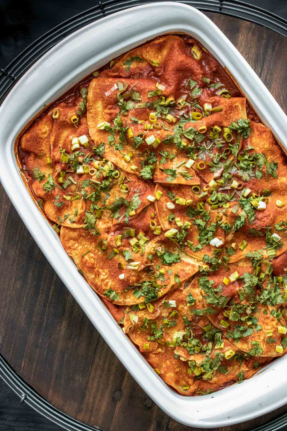 Top view of a baked layered enchilada casserole with red sauce and green onions.
