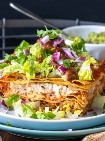 A piece of layered enchilada casserole topped with lettuce on a stack of two plates on a wooden tray.