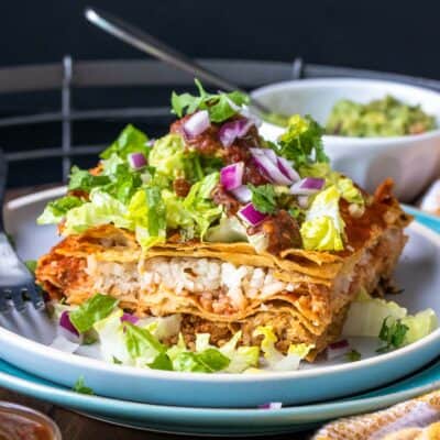 A piece of layered enchilada casserole topped with lettuce on a stack of two plates on a wooden tray.