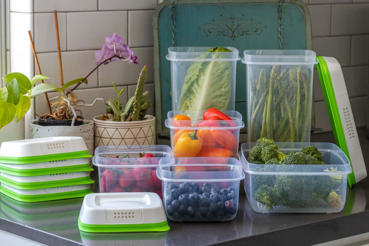 Plastic storage containers with green and white lids and produce in them on a counter.