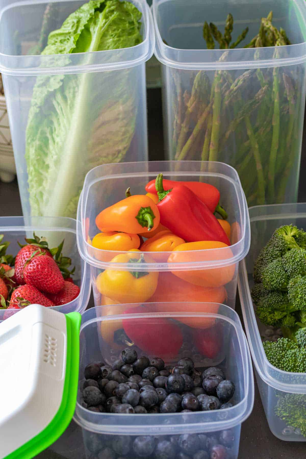 Different fruits and veggies in plastic Tupperware containers on a grey counter.