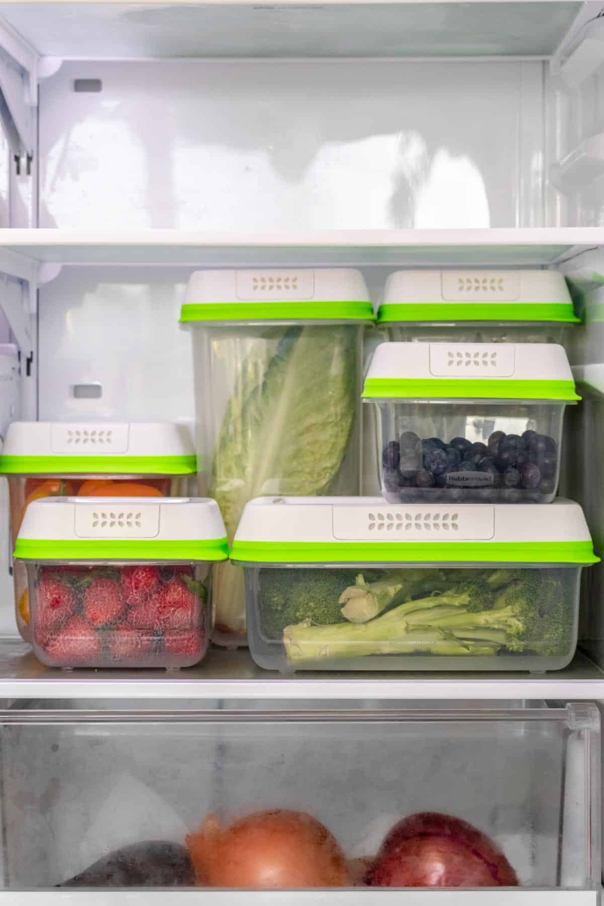 A variety of plastic containers with white and green lids stacked up on a refrigerator shelf.