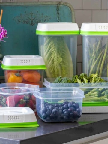 Plastic containers filled with produce on a kitchen counter, some with lids on.