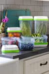 A grey kitchen counter with plastic containers containing fruits and veggies on it.