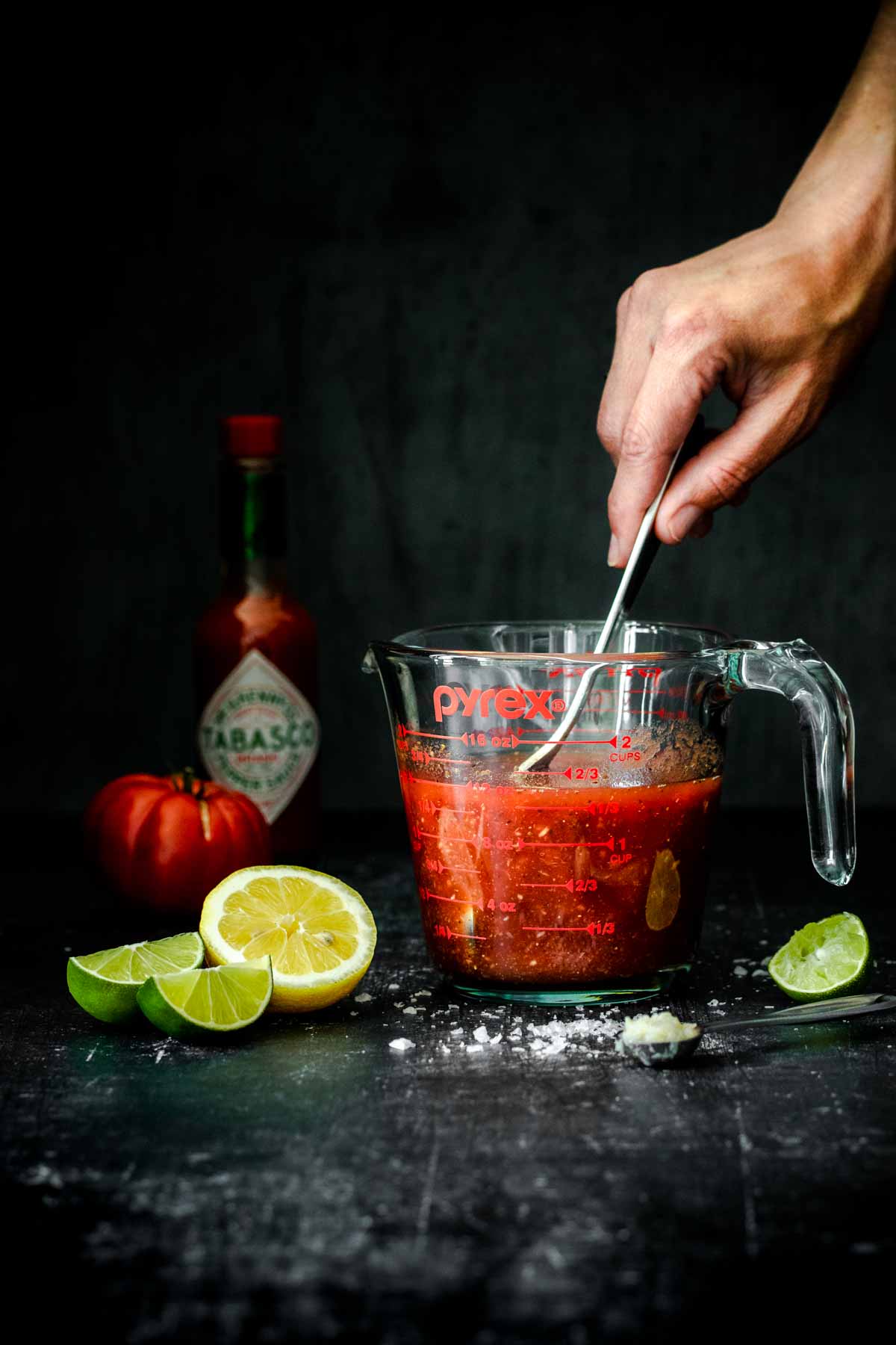 Hand mixing a red drink with a spoon in a glass measuring cup.