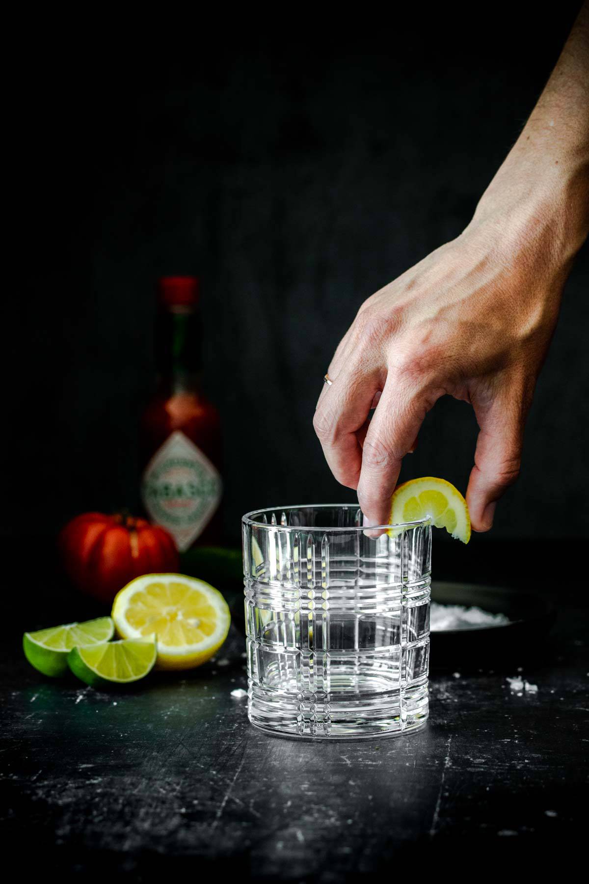 Hand using a slice of lemon to wet the rim of a lowball cocktail glass.