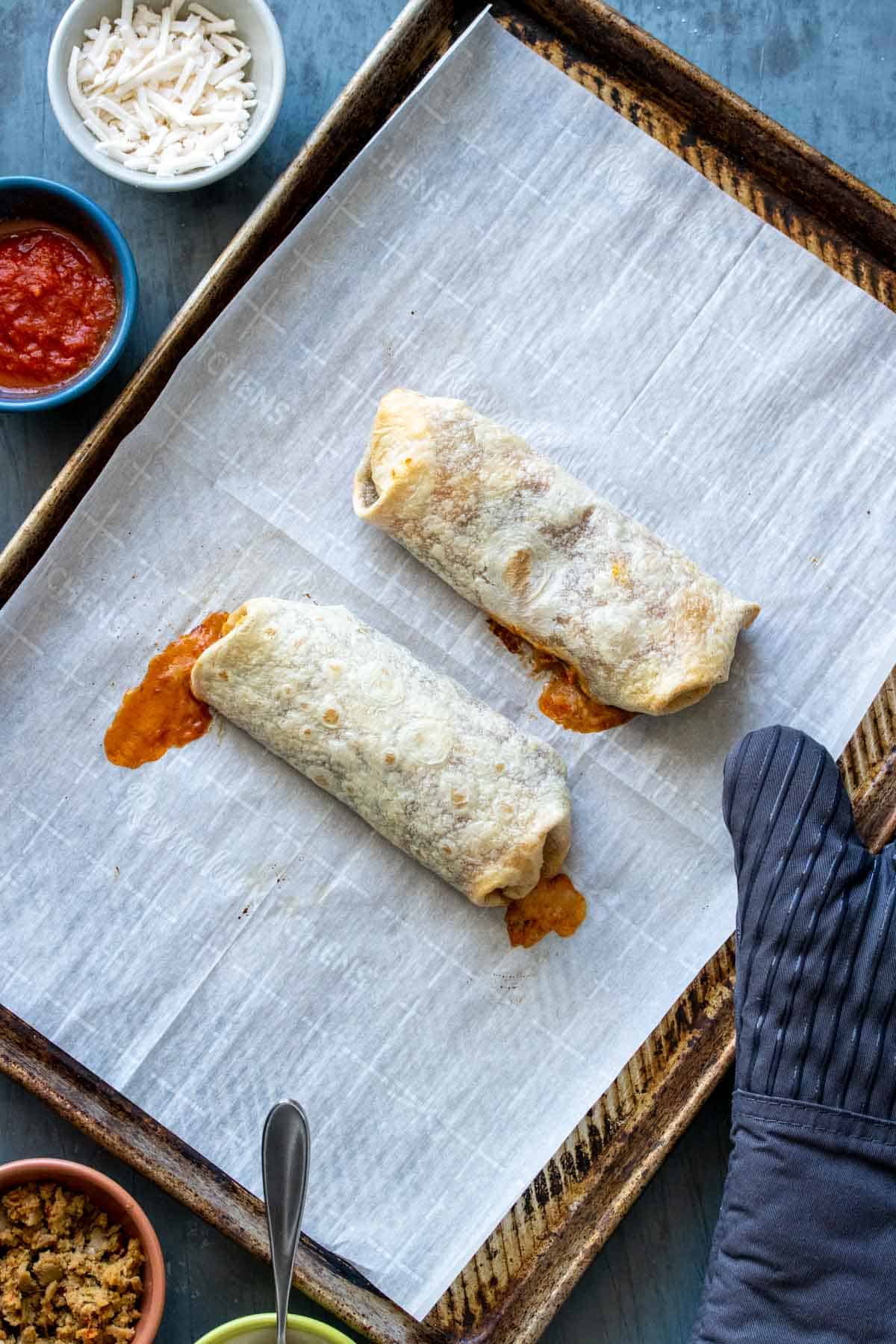 Two baked tortillas on a parchment lined baking sheet with juices spilling out the edges