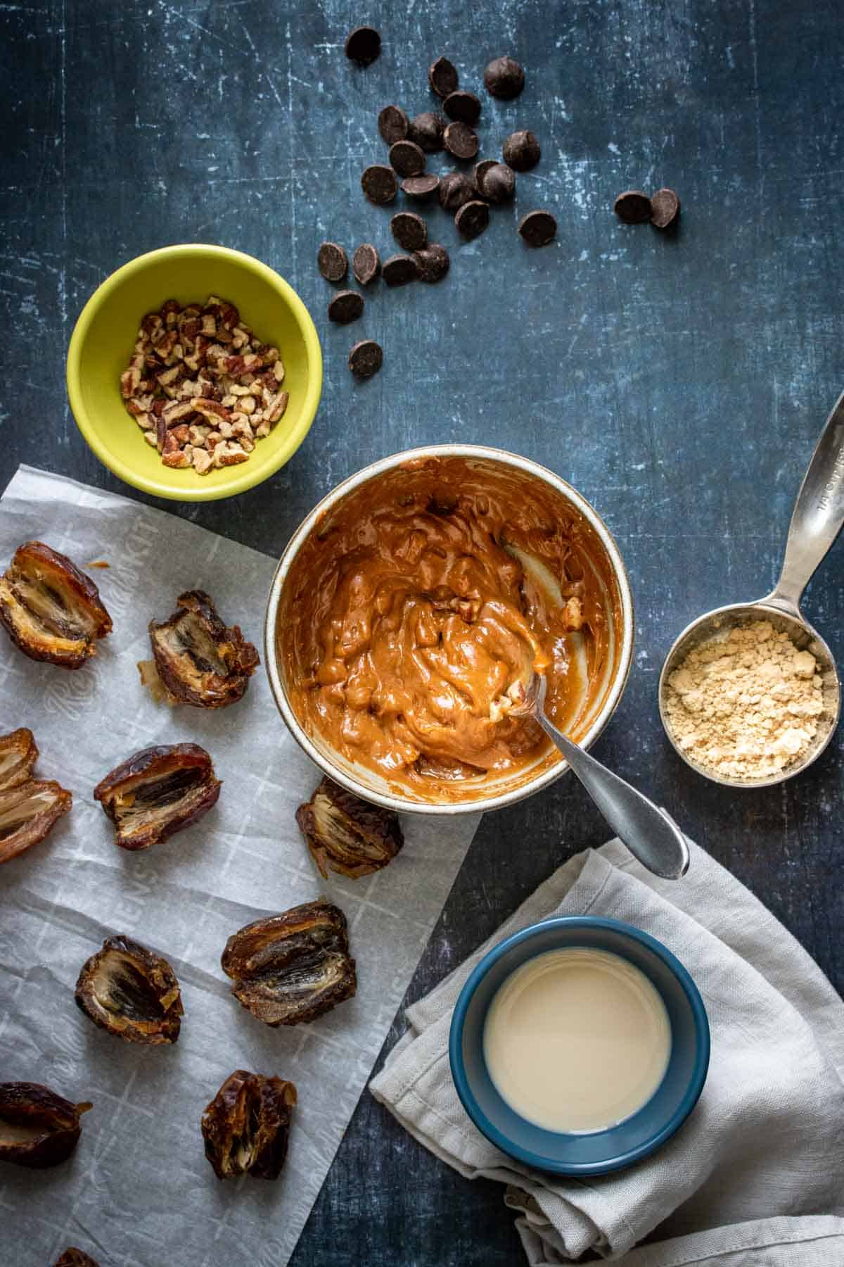 A bowl with a spoon in it mixing a creamy nut butter with pecan pieces on a dark grey surface