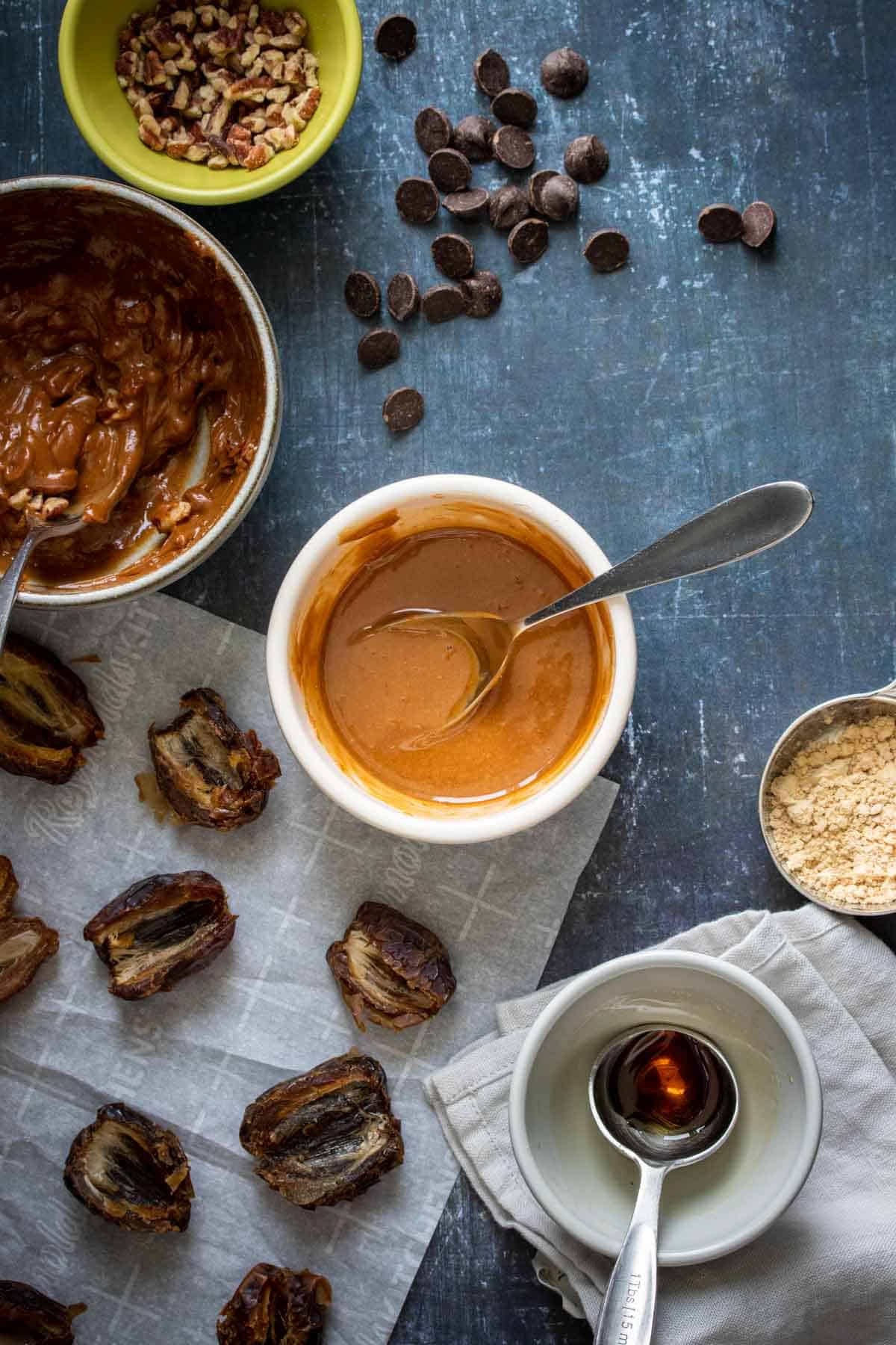 A white bowl with a spoon inside mixing a caramel looking substance next to dates and a nut butter filling