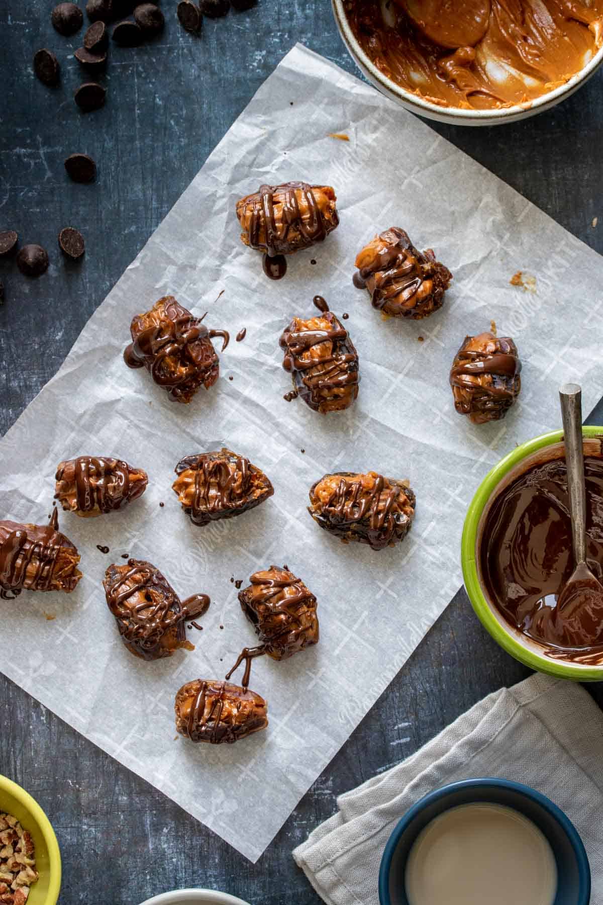 Top view of dates filled with nut butter and drizzled with chocolate on a piece of parchment paper