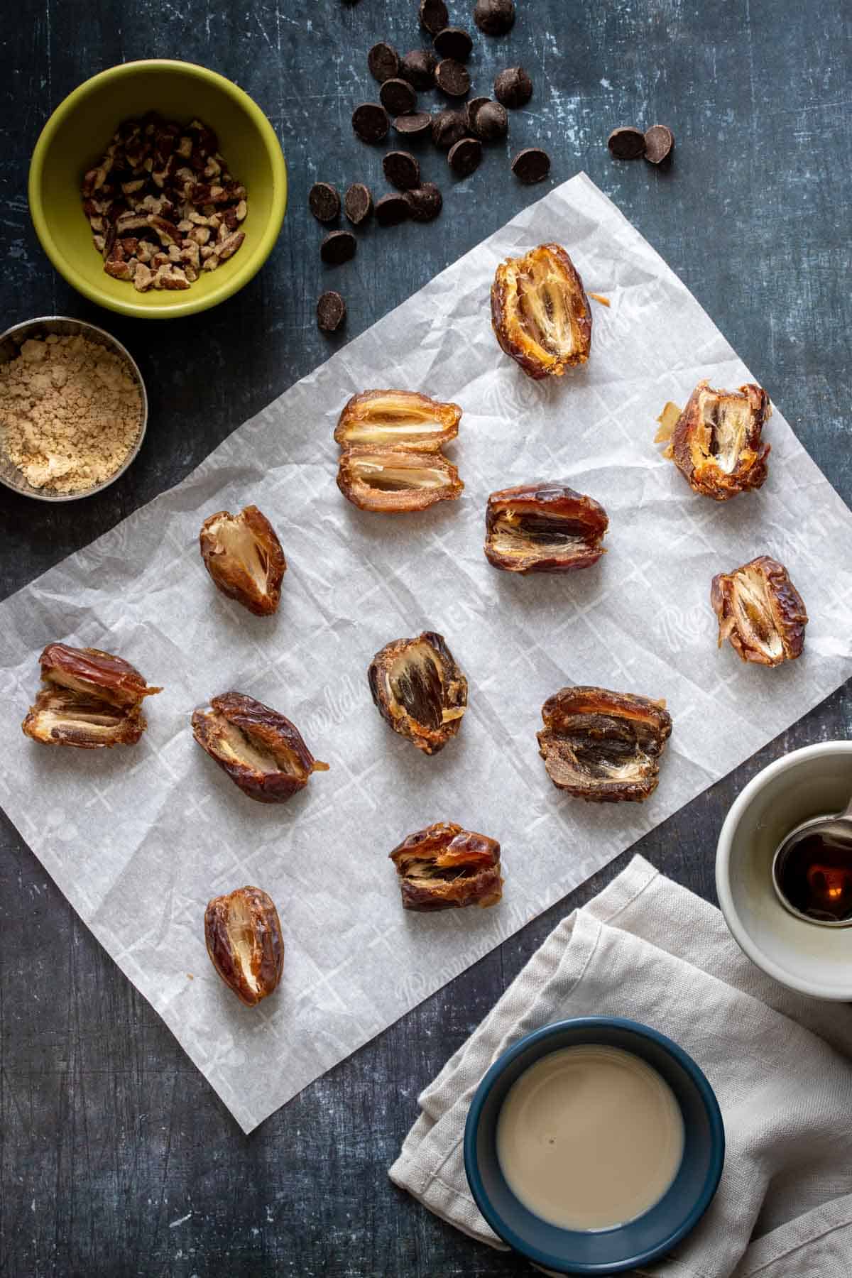 12 dates opened up on a piece of parchment paper surrounded by ingredients for a sweet filling