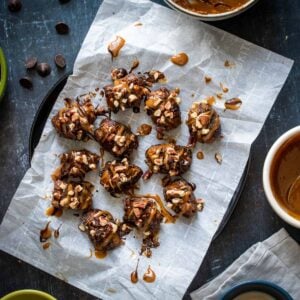 Stuffed dates topped with caramel and chocolate on a piece of parchment paper laying on a black plate